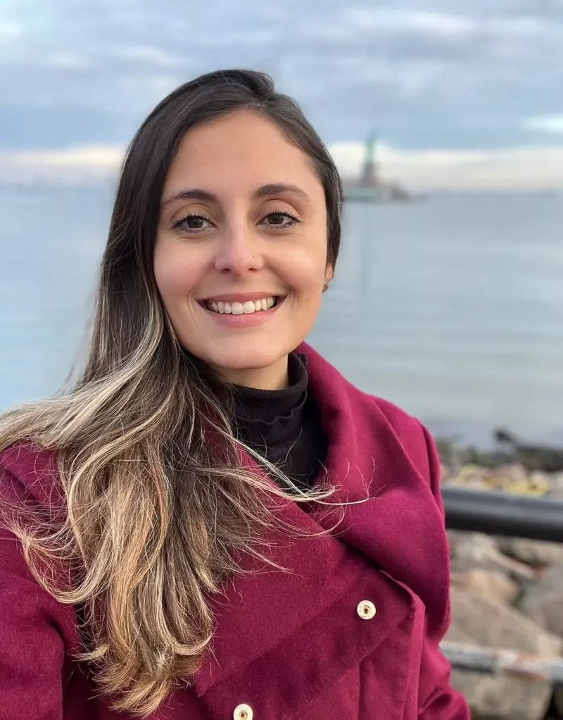 Thais Fabrini sorrindo com a Estátua da Liberdade ao fundo